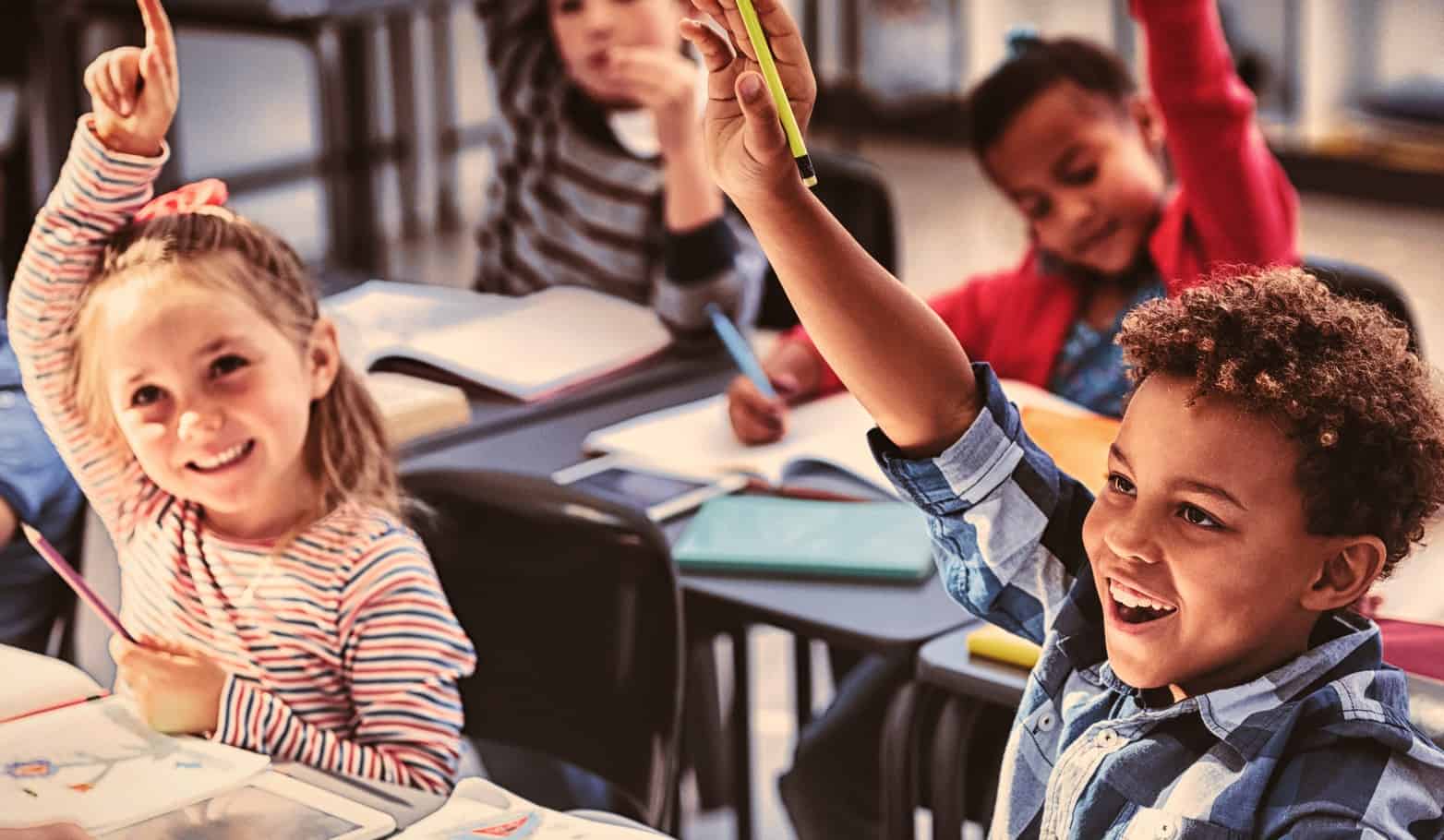 Students engaged in a classroom and raising their hands.